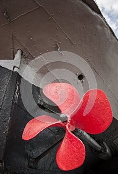 The old ship propeller is painted red. Museum piece.