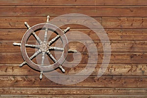 Old ship steering wheel hangs on the wooden wall