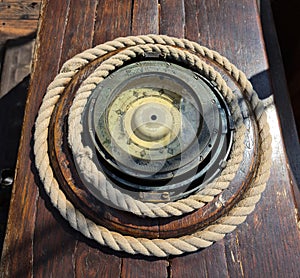 An old ship's compass on a sailboat next to the helm and a nautical rope twisted around photo