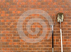 Old shovel and rake leaning red brick wall look like spoon and fork have copy space