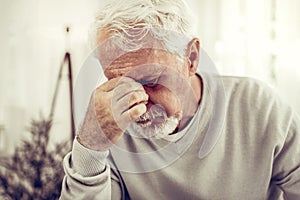 Old sick grey-haired man in beige sweater feeling terrible pain