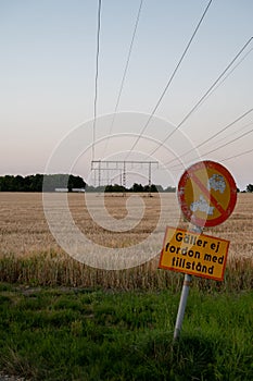 An old sign informing drivers that they are not allowed to enter the rural road next to an agricultural field with power lines in