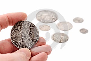 Old silver thaler in male hand and coins on white background. Lion Daalder. Selective focus