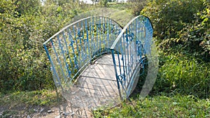 Old small blue bridge over the river. A trip to the countryside. Bent metal