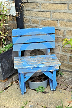 Old small blue wooden chair in a garden outside a house front