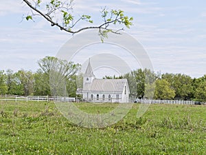 An old small white church sits next to a green pasture with summertime lighting.