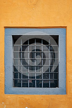 An old small window with a square lattice, like a prison on the yellow wall