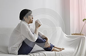 Old smart lady holding ceremic cup in hand,sitting on sofa and looking outside,relax time photo