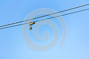 Old sneakers hanging on electrical wire with blue sky in the background