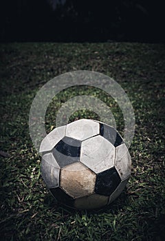 Old soccer ball or football lay on green grass for kick. Low key