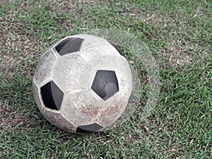 old dirty stained soccer ball made of synthetic rubber on green grass field