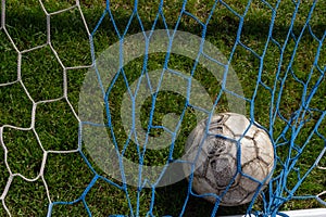 old soccer ball in the net on the background of grass soccer field. Summer sunny day