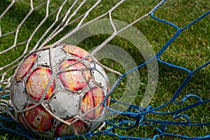 Old soccer ball in the net on the background of grass soccer field. Summer sunny day