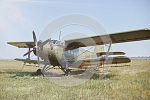 An old Soviet AN 2 aircraft of protective color stands at the airfield in a green field