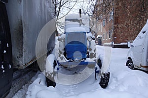 An old Soviet tractor in the snow among the cars in the parking lot