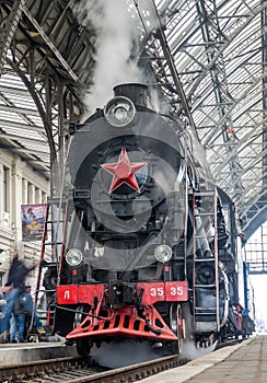 Old Soviet vintage black retro train with a red star at the railway station in Lviv produces steam from the pipes and the passeng