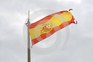 Old Spanish flag on a pole, undulating in the wind with clouds at the background, Santa Barbara castle of Alicante