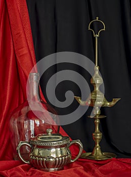 Old Spanish Oil Lamp Glass Demijohn and Silver sugar Bowl Red and Black Background Still Life