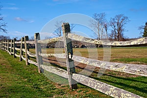 An old split-rail fence with green lichen borders a field.