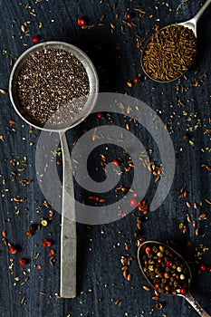 Old spoons with various seeds and spices on black background