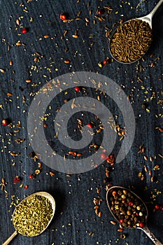 Old spoons with various seeds and spices on black background