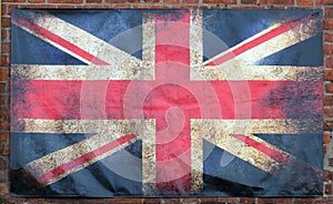 Old stained dirty union jack british flag with dark crumpled edges on a brick wall background