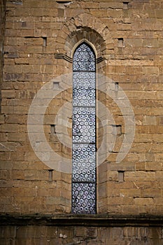Old stained-glass window in vertical narrow window of ancient brick building. Cathedral church. May, 2013. Pisa, Italy