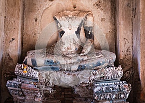 Old statue of Buddha, headless and armless. Flower garland as offering next to left foot. Destroyed and broken sculpture, ancient