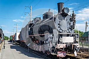 Old steam locomotive beside a railway station platform. Retro train.