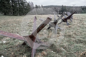 Old steel rusty anti tank roadblocks laid on grass with forest in the background on a gloomy dark day of winter without photo