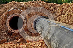 An old steel water pipe with a welded flange lies next to a new plastic pipe