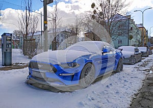 Old blue sport coupe famous car Ford Mustang parked in snow in Gdansk, March 12th, 2023.