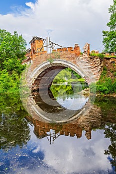 Old stone bridge arch with reflection in water, ruined historic architecture