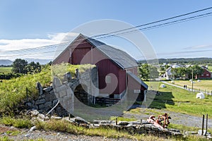 Old stone bridge connecting to a red barn surrounded by greenery and short trees in Alesund, Norway