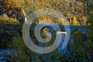 Old stone bridge over the mountain river across autumn forest, hills, and sunset sky. Natural background. Travel, movement, archit