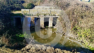 Old stone bridge over stream with dirty water, in Vitigudino, Spain.