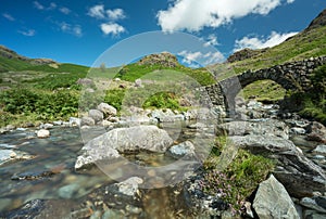 Old stone bridge in remote Lake District nature, with stream and blue skies