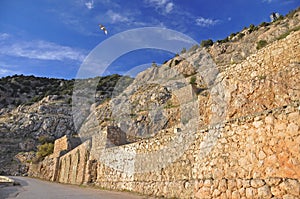 The old stone fortified wall stands high in the mountains against the blue sky