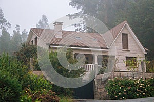 Old stone house with beautiful garden in morning fog. Rural cottage in village in forest. Cozy residence with trees and flowers.