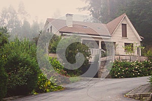 Old stone house with beautiful garden in morning fog. Rural cottage in village in forest. Cozy residence with trees and flowers.