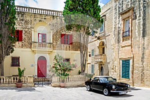 Old stone house with colorful windows and black classic style convertible car - Mdina, Malta