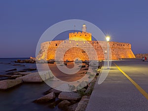 Old stone lighthouse in Fort St. Nicholas in Rhodes at sunset.