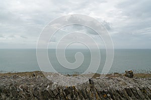 Old stone rock wall and view over an expanisve ocean under an overcast sky