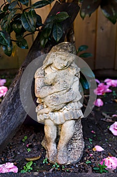 Old Stone scupture of girl holding cat under camelia bush.