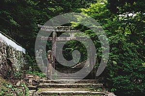 Old stone torri gate over a stairs path in park on Mount Misen in Miyajima, Hiroshima, Japan