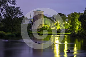 Old stone tower of medieval fortress and small church reflecting in river at night. Pskov fortifications, Russia