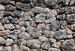 Old stone wall consisting of stacked naturally shaped loose rocks - background pattern