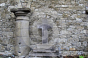 Old stone wall with graveyard cross and column resting against it