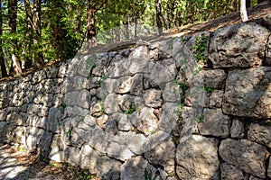 An old stone wall made of rough stone. An ancient fortified wall fence with a pattern of green grass and moss.