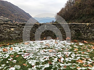 old stone wall with snow and leaves in front is a viewpoint of the mountains